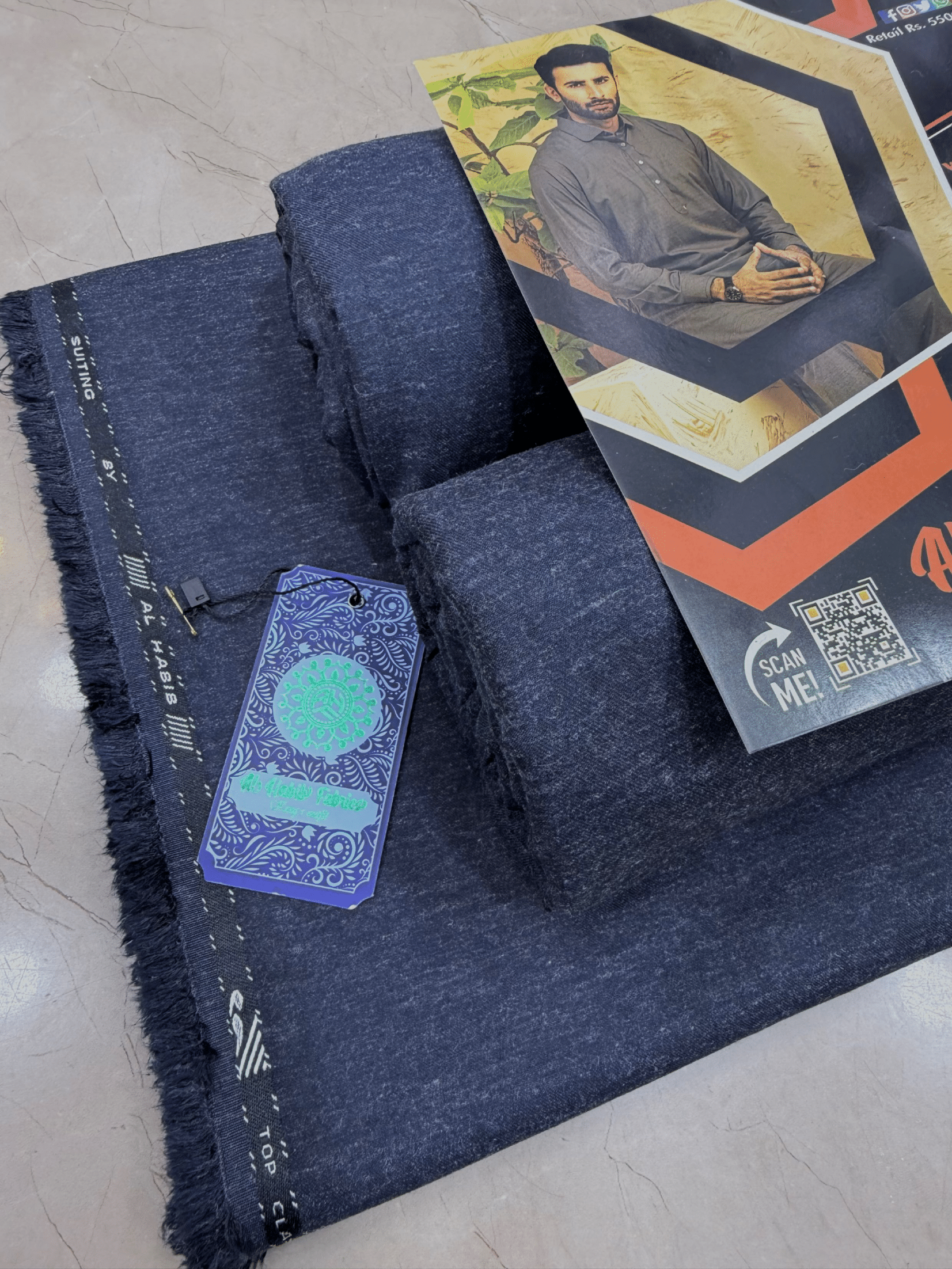 Dark blue fabric with a tag and promotional material on a light gray surface**AlHabibFabrics, AlHabibWinter, King'sOutfit, TopClassChoice, AlHabib, KashmirWool, WoolFabric, PremiumWool, SoftWool, WarmFabric, UnstitchedWool, SuitingWool, Men'sSuiting, UnstitchedFabric, ShalwarKameezFabric, KurtaShalwarFabric, Men'sDressMaterial, PremiumSuit, LuxuryMenswear, ElegantFabric, FormalWearMen, BestWinterFabric, NavyBlue, CharcoalGrey, DarkBrown, DeepBlue, MaroonFabric, GreySuit, PlainColors, PakistaniFabric, Menswe