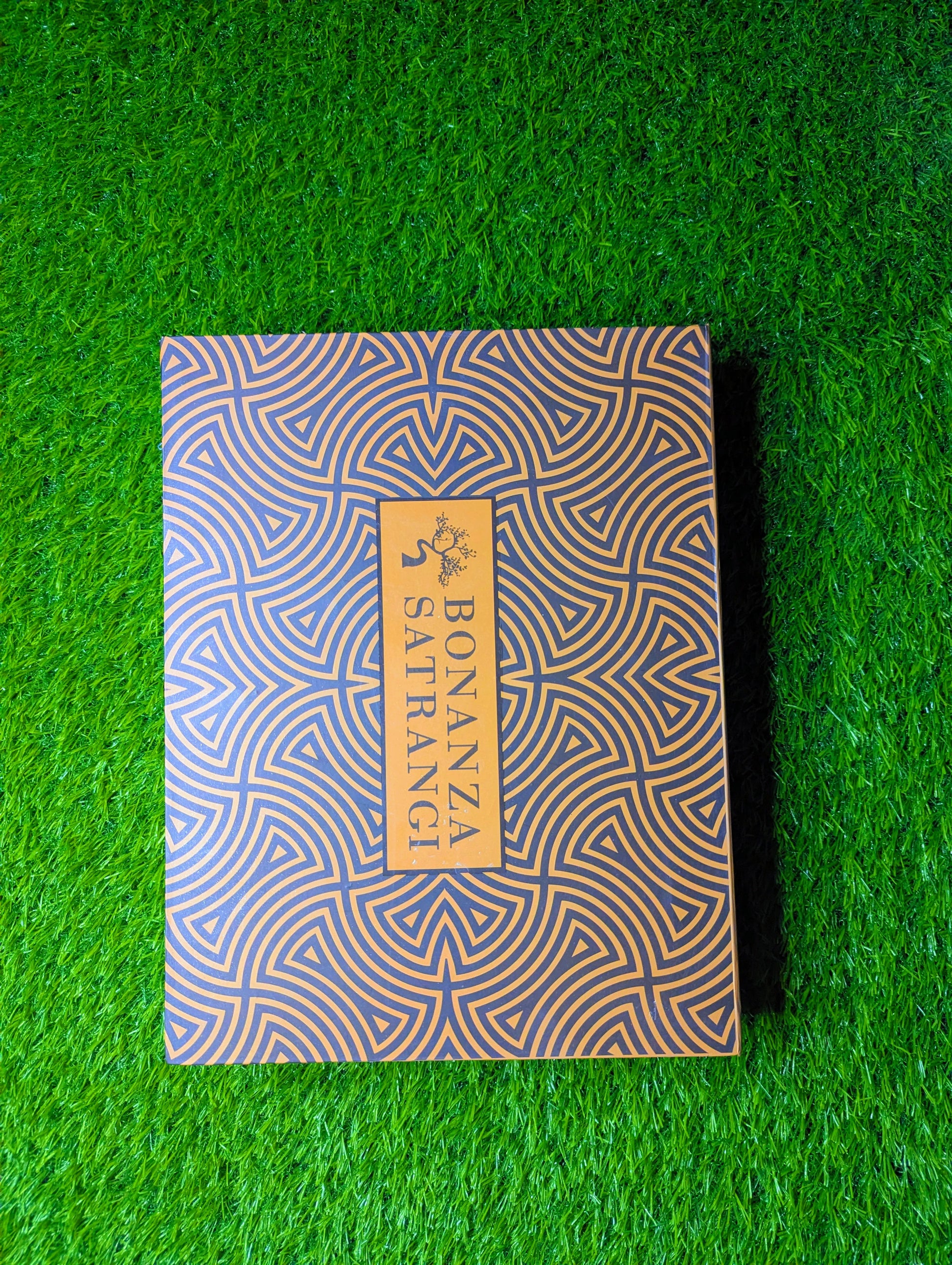 Notebook with geometric pattern and 'Bonanza Satrangi' branding on a green grass backgroundn a gray outfit.Bonanza Satrangi Unstitched, Bonanza Satrangi Men's Fabric, Bonanza Satrangi Gents SuitMen's Wash & Wear Fabric, Unstitched Shalwar Kameez, Gents Wash n Wear Suit, Premium Wash and Wear FabricWrinkle-Free Fabric, Easy Care Fabric, Low Maintenance SuitShalwar Kameez Fabric Price, Wash n Wear Price in Pakistan, Gents Unstitched Suit PK